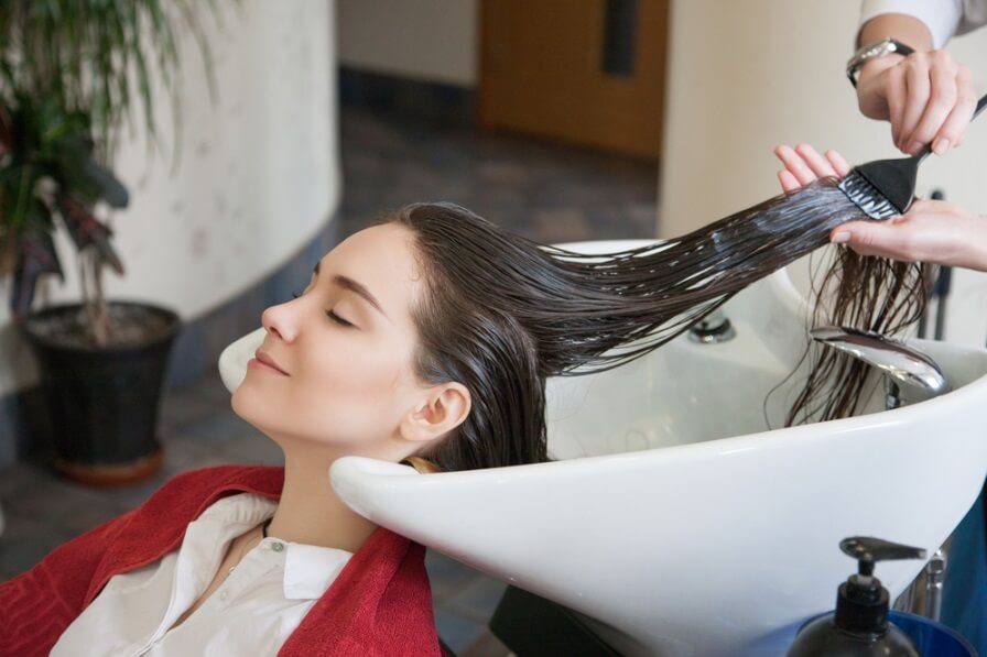 Không gian salon tóc chuyên nghiệp, kỹ thuật viên đang thực hiện liệu trình hấp phục hồi tóc nhuộm